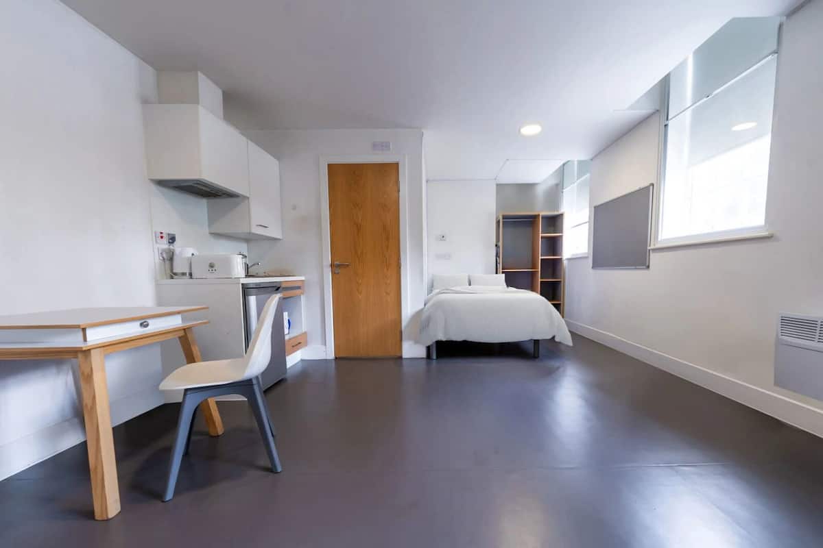 Une petite pièce comprenant un coin cuisine, un lit, un bureau et une chaise.