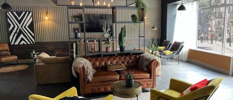 Een moderne woonkamer met een leren bank, gele stoelen, een televisie en een plantenplank.
