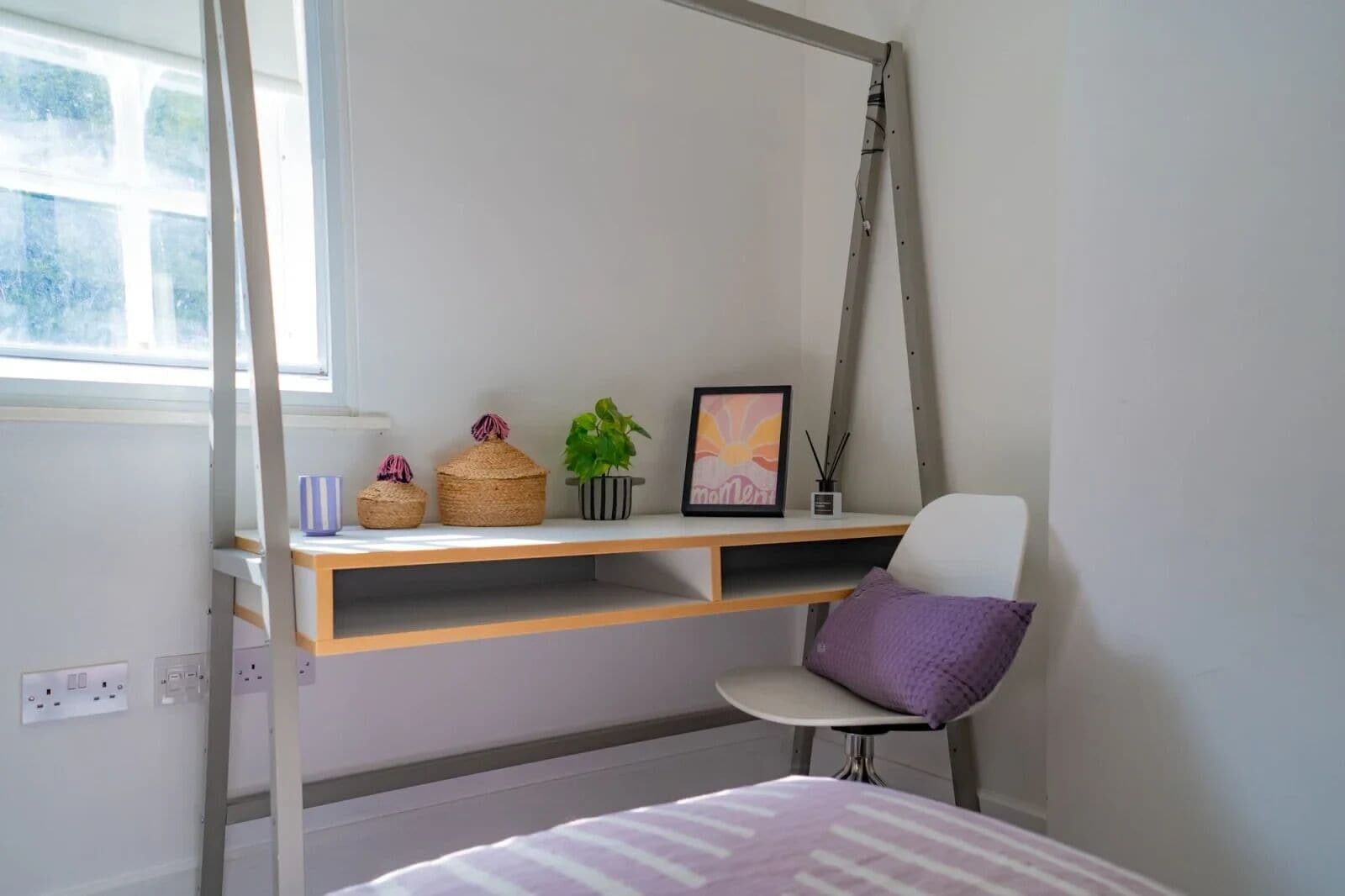 Un dormitorio con una cama, un escritorio con silla, una ventana y una escalera.