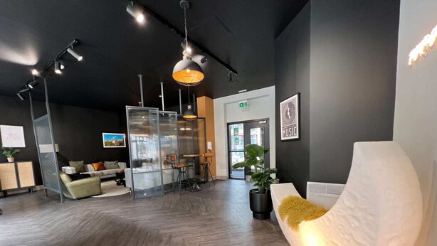 A modern reception area with a wooden floor, a seating area with a sofa and chairs, a large potted plant, and a wall-mounted sign that reads "MUSIC". - Student Only Canvas The Old Fire Station Birmingham (Birmingham)