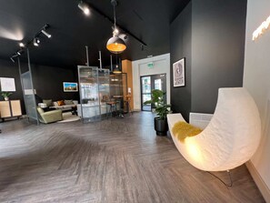 A modern reception area with a wooden floor, a seating area with a sofa and chairs, a large potted plant, and a wall-mounted sign that reads "MUSIC". - Student Only Canvas The Old Fire Station Birmingham (Birmingham)