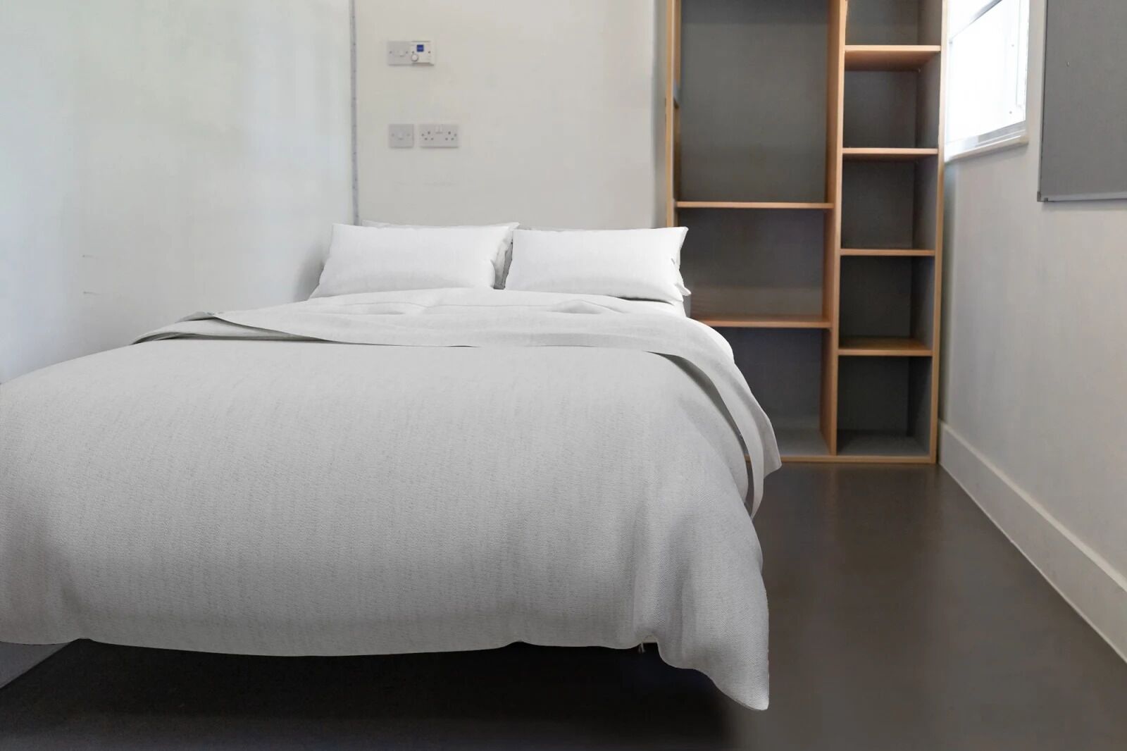 A minimalist bedroom with a bed, a built-in shelving unit, and a window.