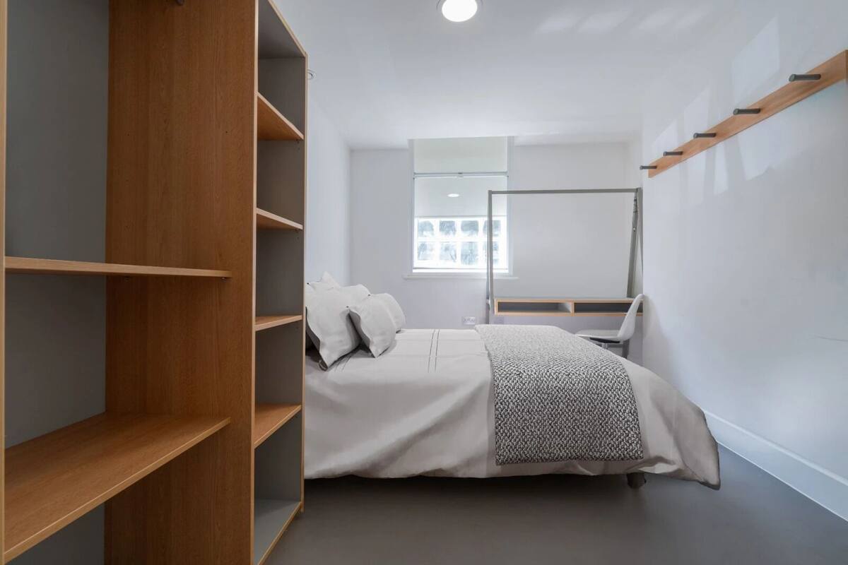 Une chambre à coucher avec un lit, une armoire en bois, un bureau et une fenêtre.