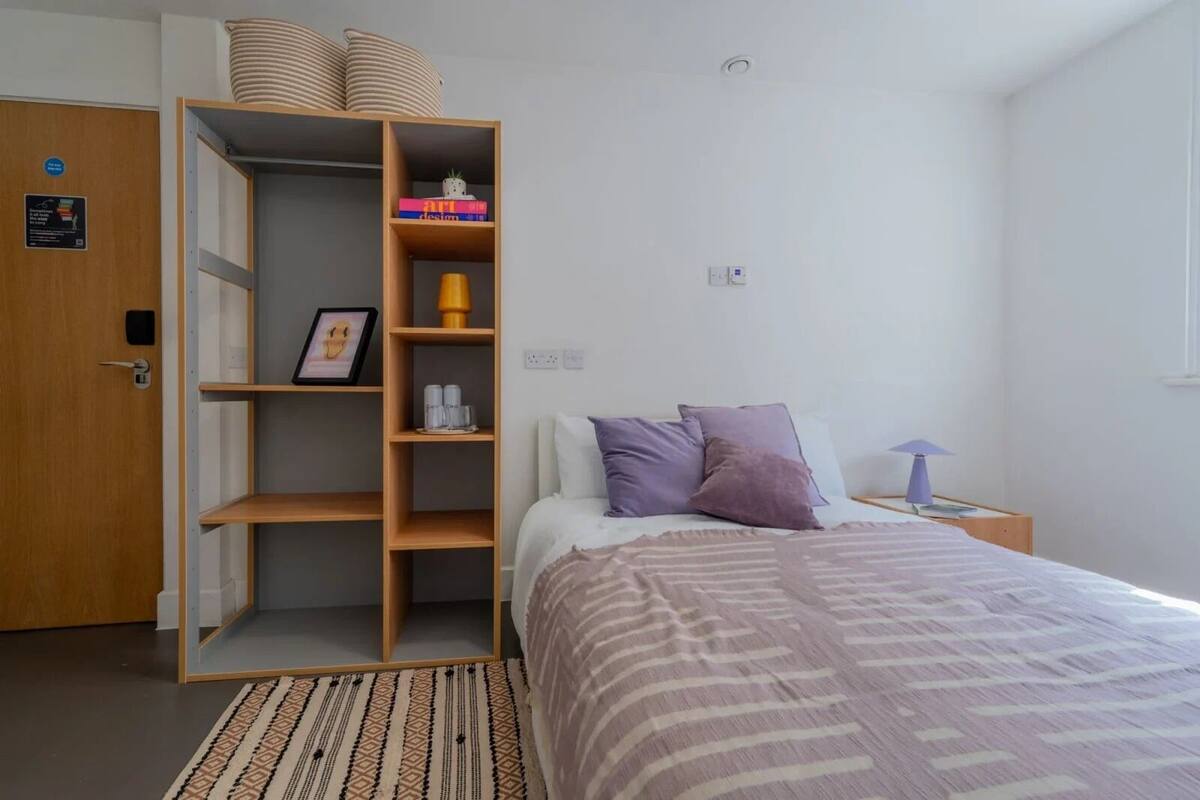 Une chambre à coucher comprenant un lit, une table de chevet, une lampe, une armoire et un tapis à motifs.