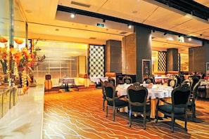 A banquet hall with round tables and chairs, a patterned carpet, and a decorative wall. - Inner Mongolia Uiles Hotel (Hohhot)