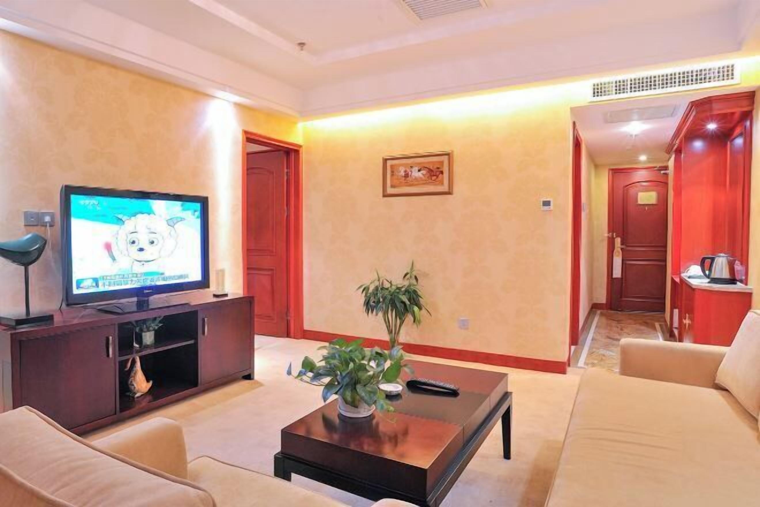 A living room with a television, sofa, coffee table, and a plant.