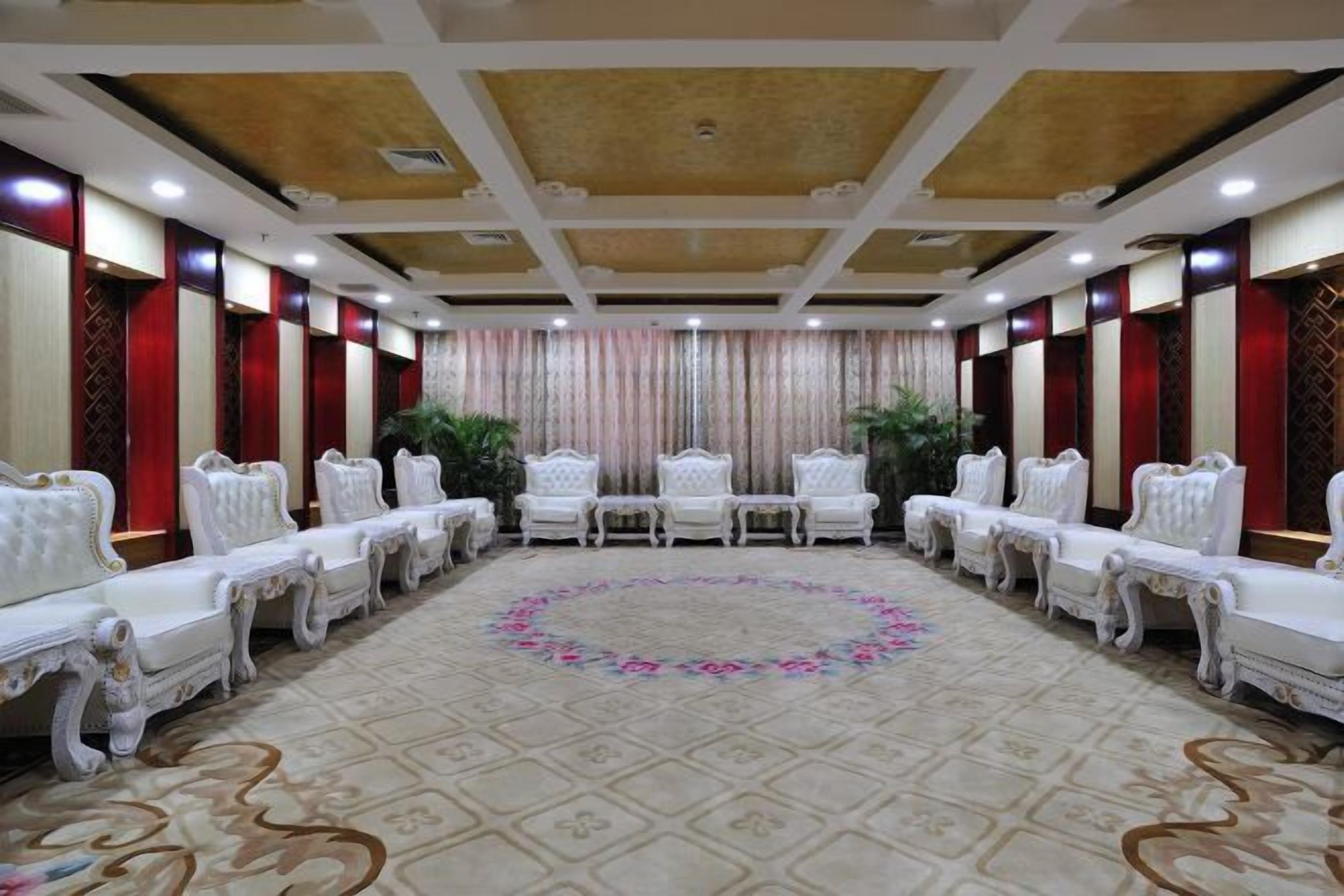 A conference room with a patterned carpet, white upholstered chairs, and a decorative ceiling.