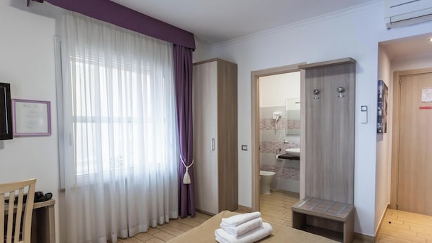 A hotel room with a bed, a desk, a chair, a bathroom visible through an open door, and a window with curtains. - Hotiday Room Collection - Roma Barberini (Rome)