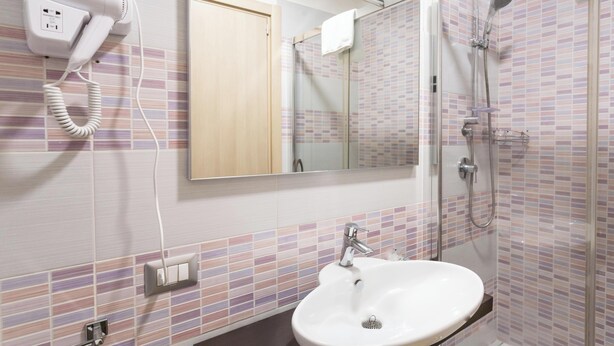 A bathroom with a white sink, a glass shower enclosure, a hairdryer on the wall, and a mirror above the sink. - Hotiday Room Collection - Roma Barberini (Rome)