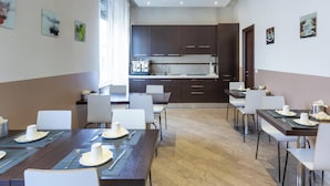 A modern dining area with multiple tables and chairs, a kitchen in the background, and artwork on the walls. - Hotiday Room Collection - Roma Barberini (Rome)