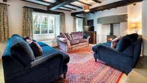 A cozy living room with dark blue sofas, a patterned rug, and exposed wooden beams.