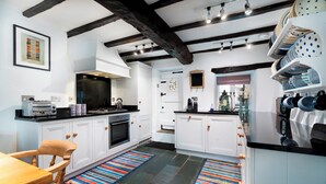 A modern kitchen with white cabinets, a black countertop, and a wooden chair. There are colorful striped rugs on the floor.