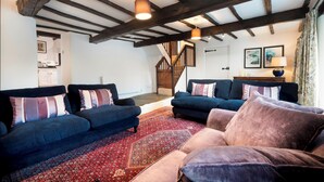 A living room with dark blue sofas, a red patterned rug, and exposed wooden beams on the ceiling.