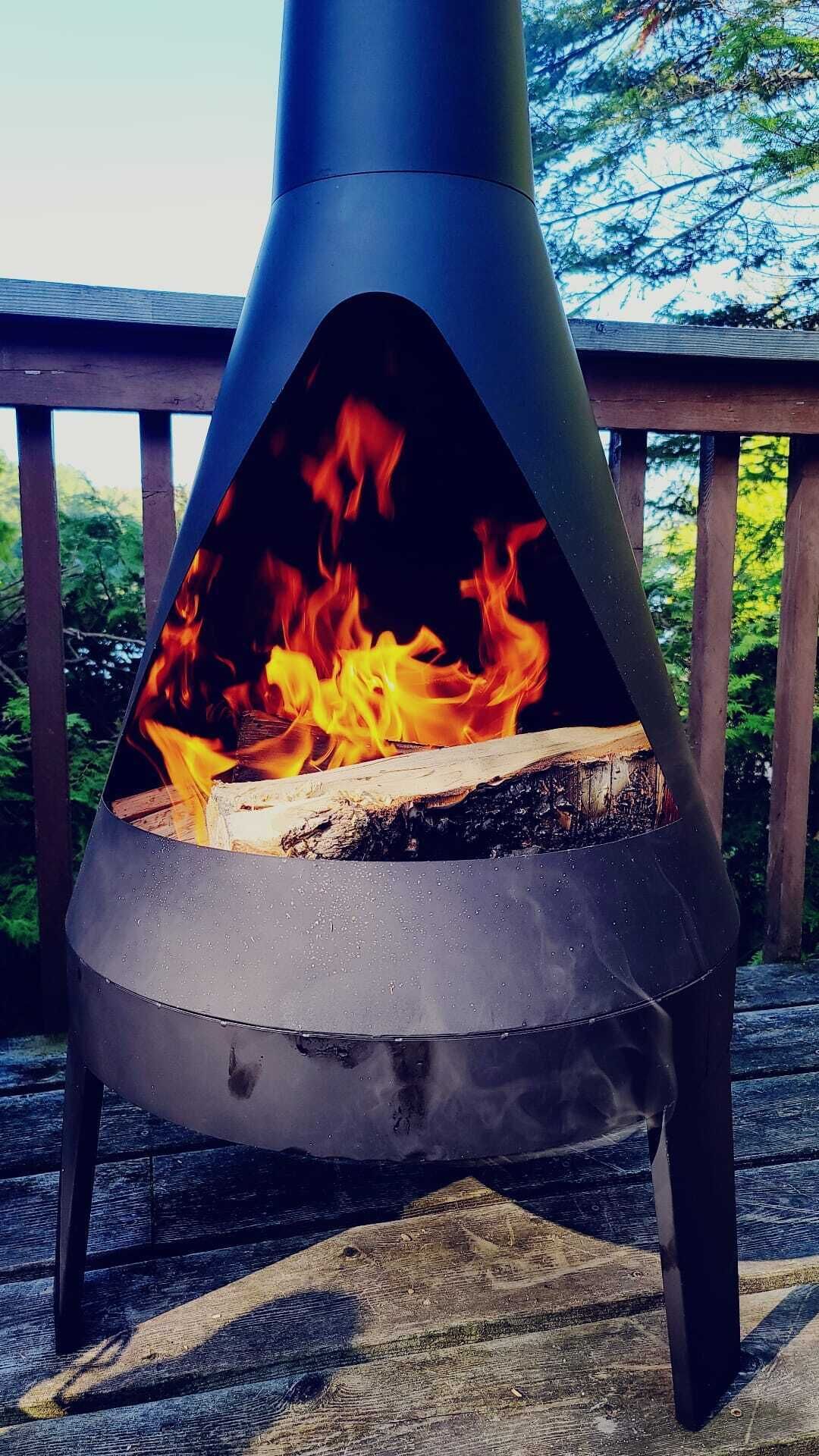 A metal outdoor fire pit with flames, set on a wooden deck with a railing.