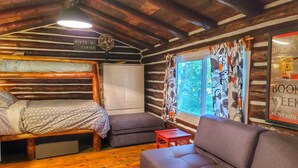 A cabin interior with a bed, sofa, and a window with curtains. - Birch Cabin- North Frontenac Lodge (Ompah)