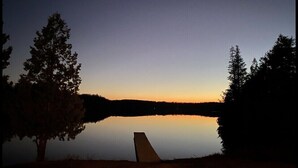 A serene lakeside scene at dusk with a clear sky, calm water, and a single chair by the water's edge. - Birch Cabin- North Frontenac Lodge (Ompah)