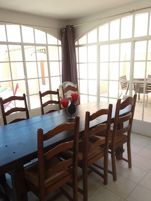 A dining area with a wooden table and chairs, large windows with curtains, and a fan. - Spacious house, private pool, 4 bedrooms, Vallon-Pont-d'Arc, Ardèche (VALLON PONT D'ARC)