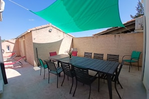 An outdoor patio with a table and chairs, a green shade sail, and a brick wall. - Spacious house, private pool, 4 bedrooms, Vallon-Pont-d'Arc, Ardèche (VALLON PONT D'ARC)