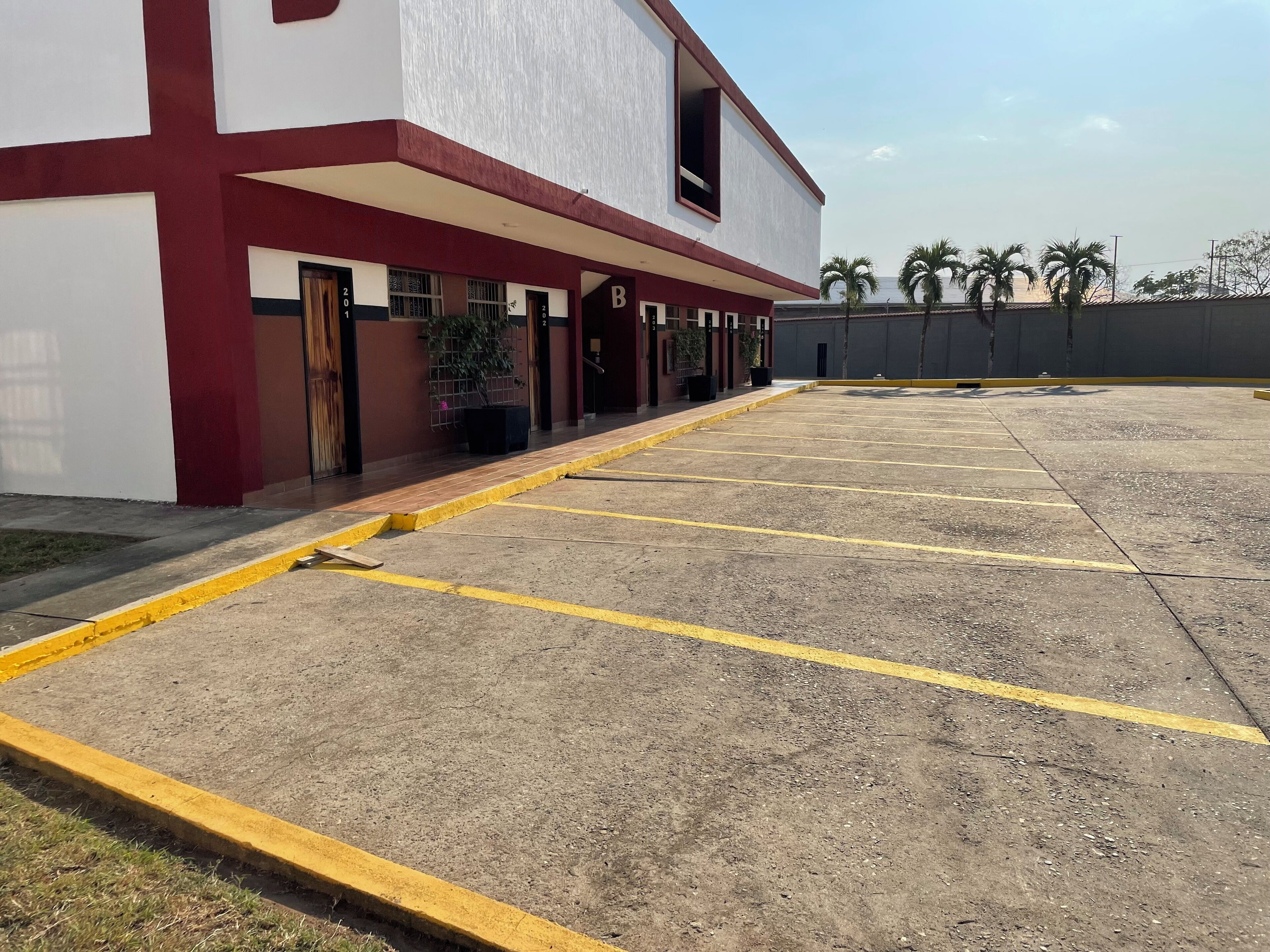 A building with a red and white facade, a covered parking area with yellow lines, and a palm tree in the background.