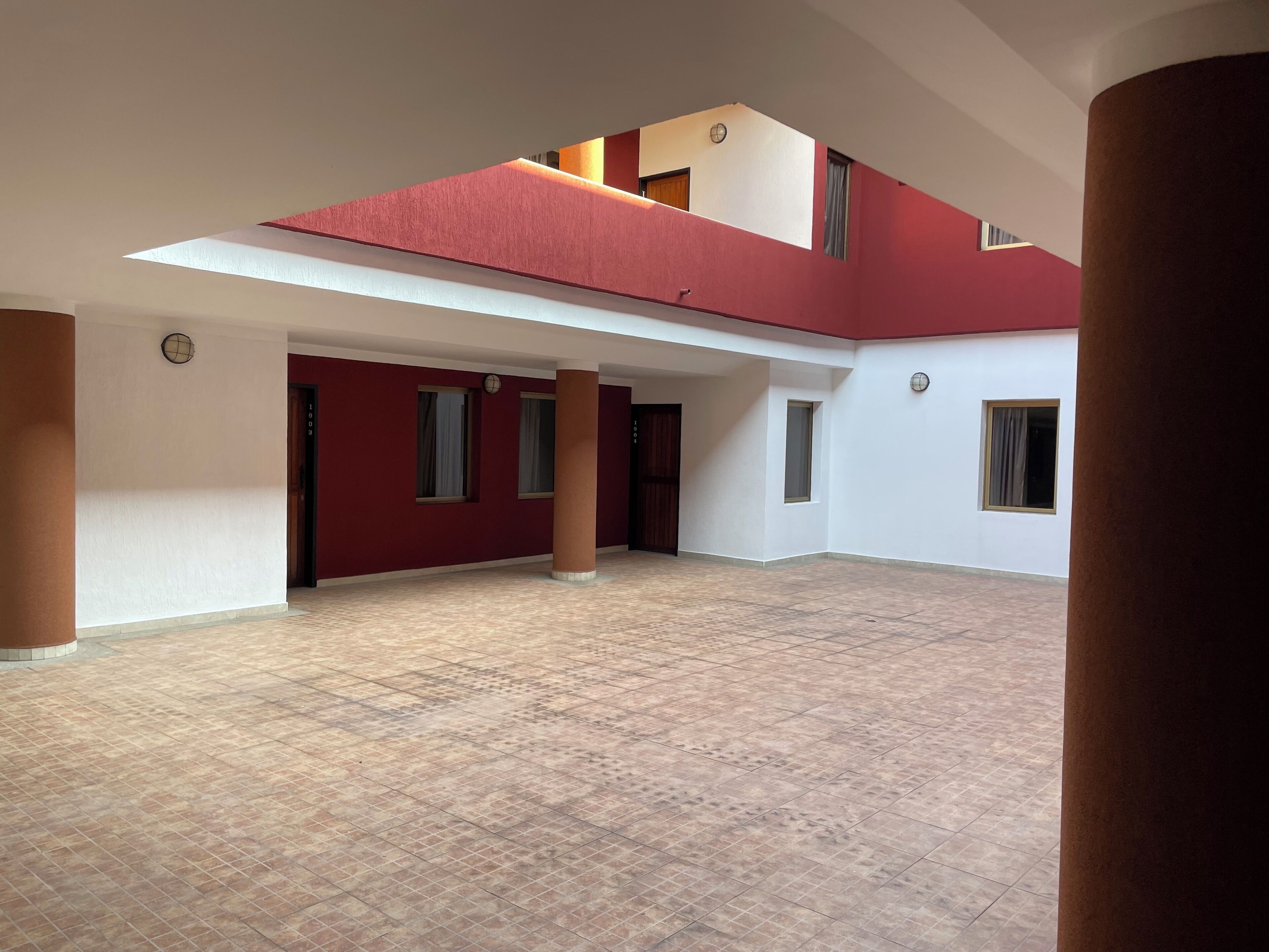 Un vaste espace intérieur doté d’un sol carrelé, de murs rouges et de nombreuses fenêtres.