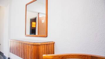 A wooden bench and a mirror in a hallway with white walls.