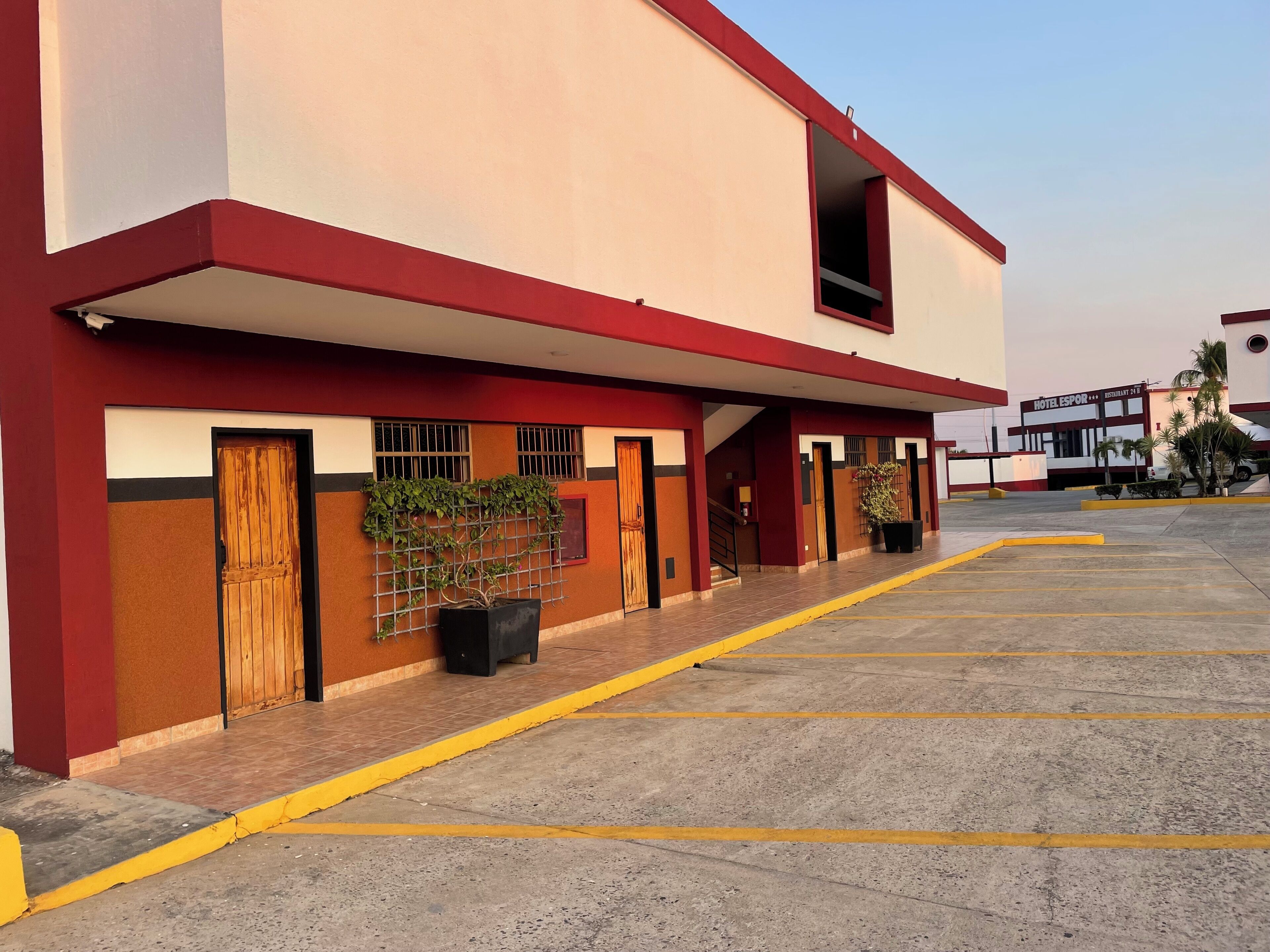 Un hotel con fachada roja y blanca, varias puertas y un estacionamiento.