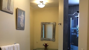 A bathroom with a towel rack, a mirror, a vanity with a vase of flowers, and a door leading to another room. - Hotel Posada San Miguel (Jerez de García Salinas)