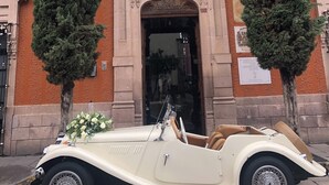 A vintage convertible car parked in front of a building with ornate architecture and two tall trees. - Hotel Posada San Miguel (Jerez de García Salinas)