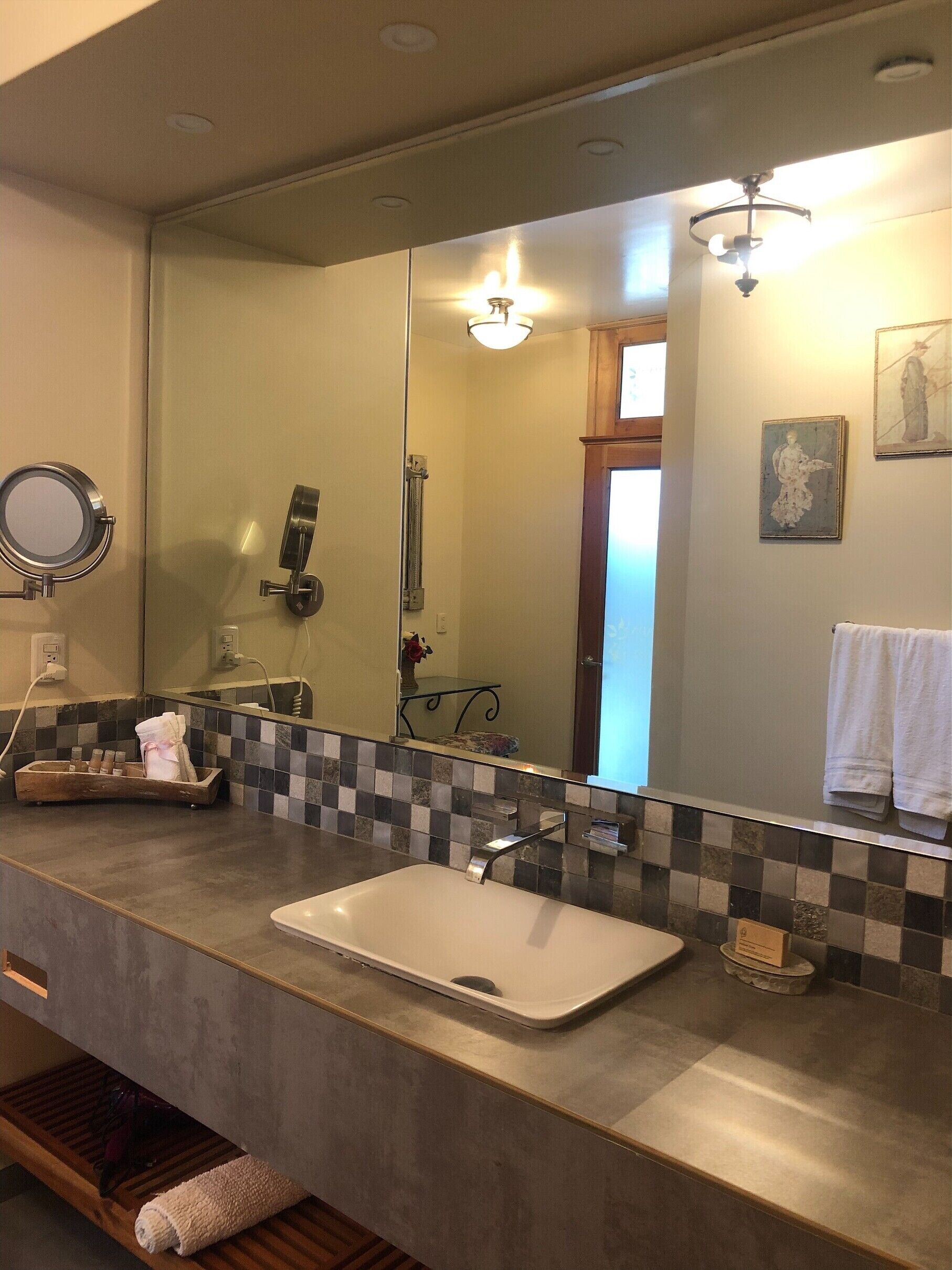 Un baño con un espejo grande, un lavamanos, un perchero para toallas y una zona de ducha.