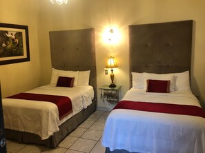 A hotel room with two single beds, each with white linens and red throw pillows, a nightstand with a lamp, and a framed picture on the wall. - Hotel Posada San Miguel (Jerez de García Salinas)