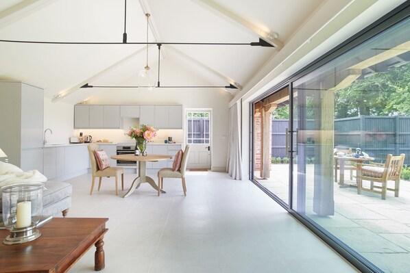 A modern kitchen with white cabinets, a dining area with a table and chairs, and a large sliding glass door leading to an outdoor patio.