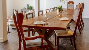 Una larga mesa de madera con sillas, un televisor montado en la pared y un cuadro enmarcado sobre la mesa.