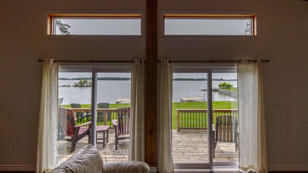 Una habitación con un amplio ventanal corredizo que da a una terraza con mobiliario exterior y vista a un lago.