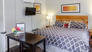 Una camera da letto ordinata con un letto, un comodino, una lampada e una piccola scrivania con una sedia.