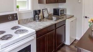 Una cucina con mobili bianchi, un fornello bianco, un forno a microonde e un lavello.