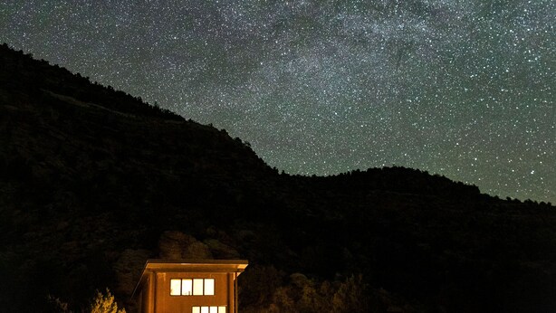 Ein Haus unter einem Sternenhimmel, umgeben von einem Wald.