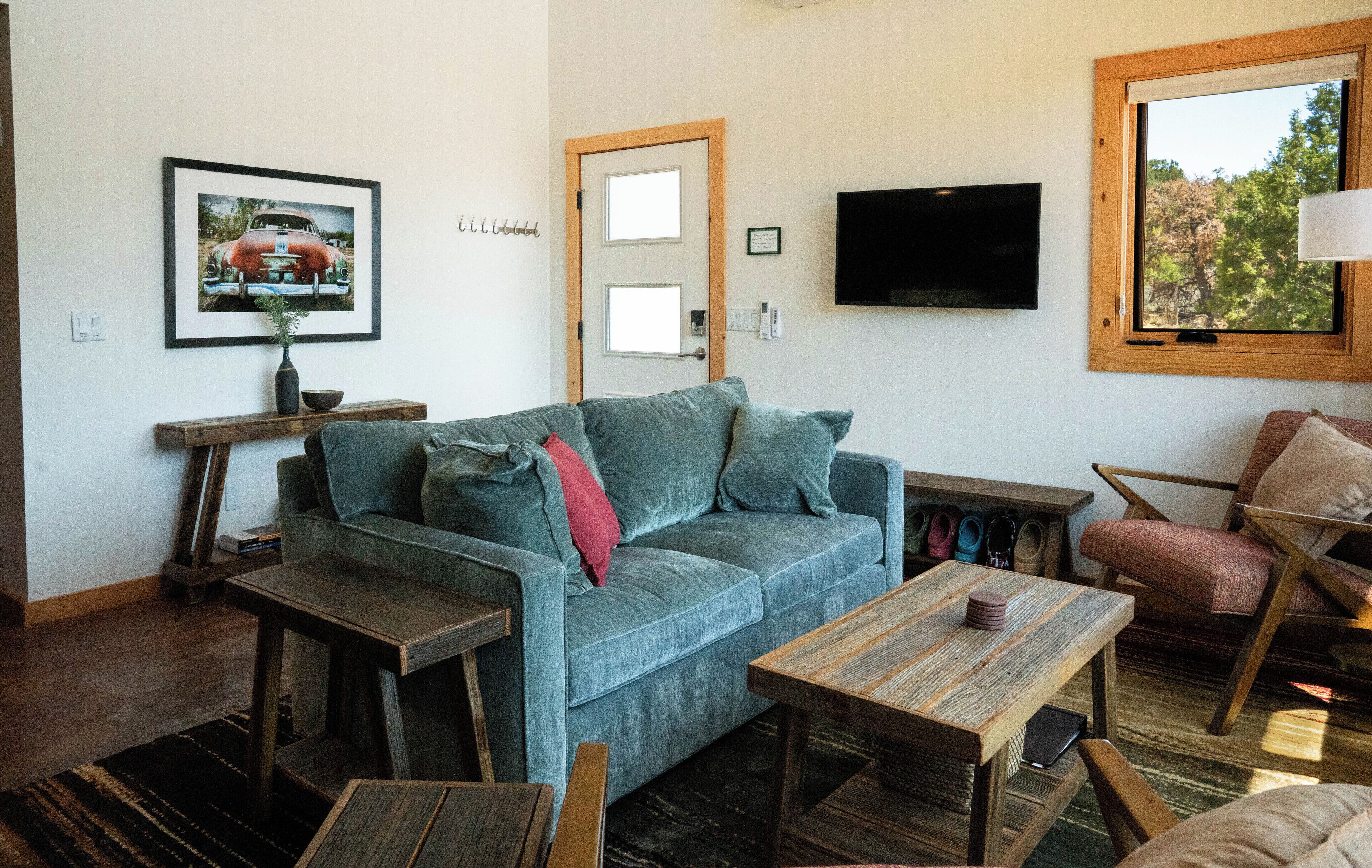 A living room with a sofa, coffee table, and armchair, a TV mounted on the wall, and a door with a window.
