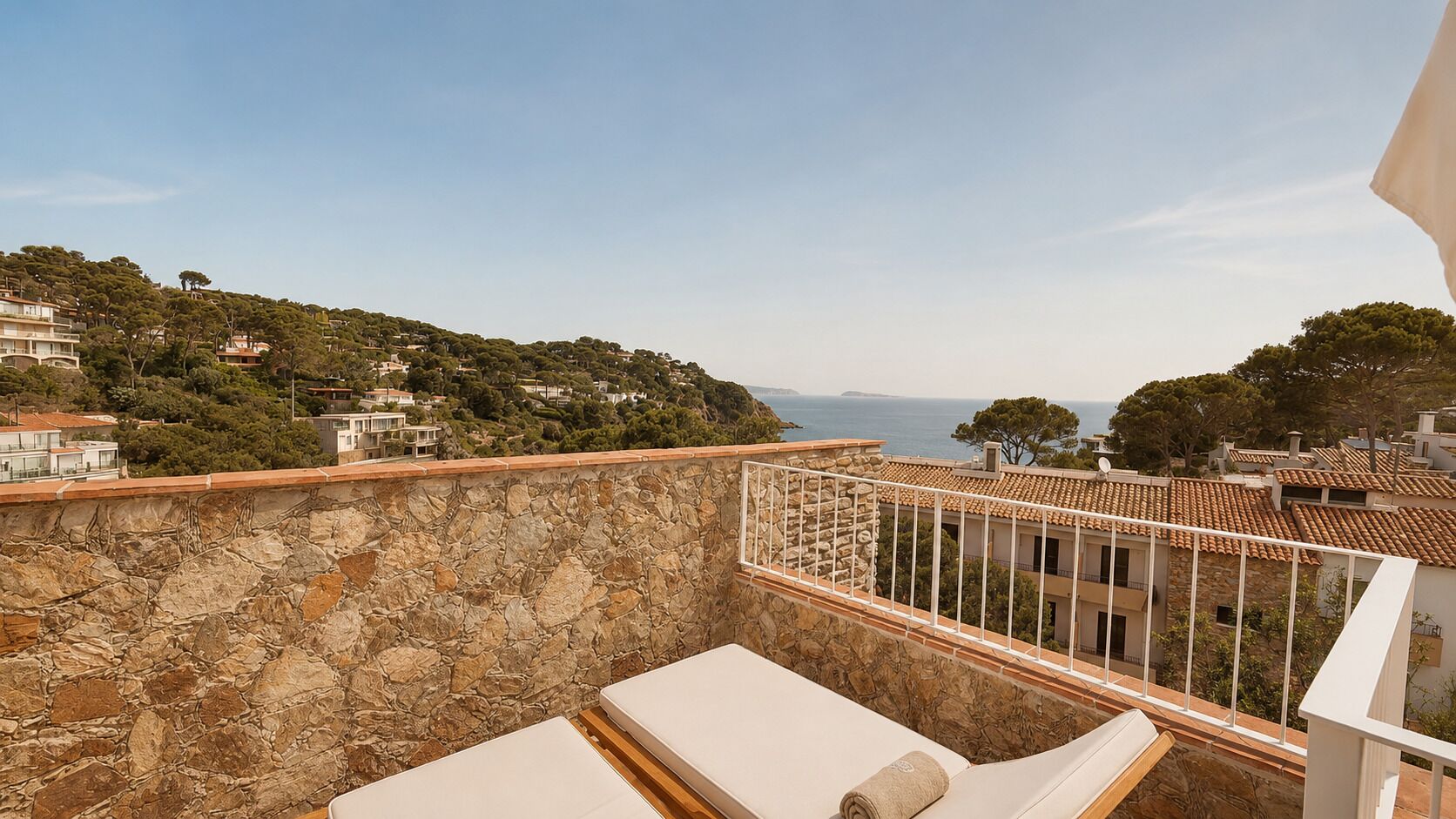 Un balcon doté de murs en pierre, de balustrades blanches et offrant une vue sur une ville côtière.