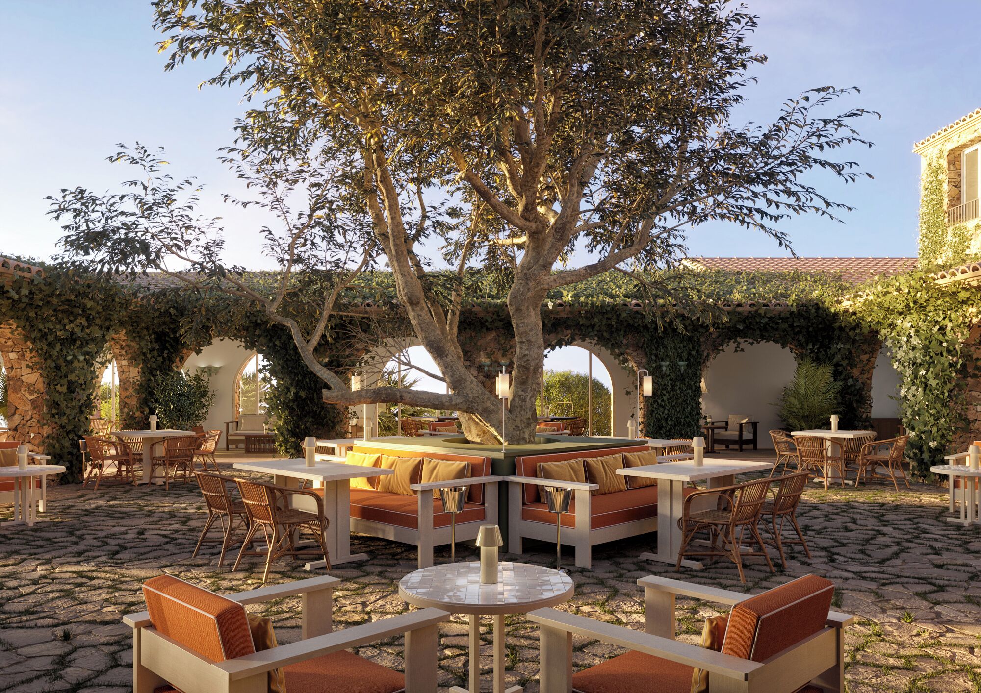 Zona relax all'aperto con tavoli rotondi e panche imbottite, circondata da mura in pietra e coperta da una pergola ricoperta di vite.