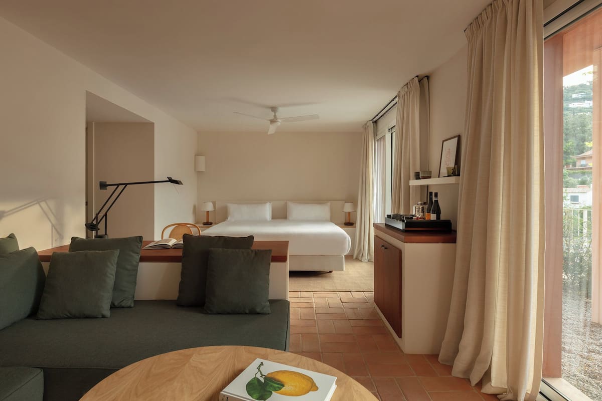 A hotel room with a bed, a sofa, a dining area, and a view of the outdoors.