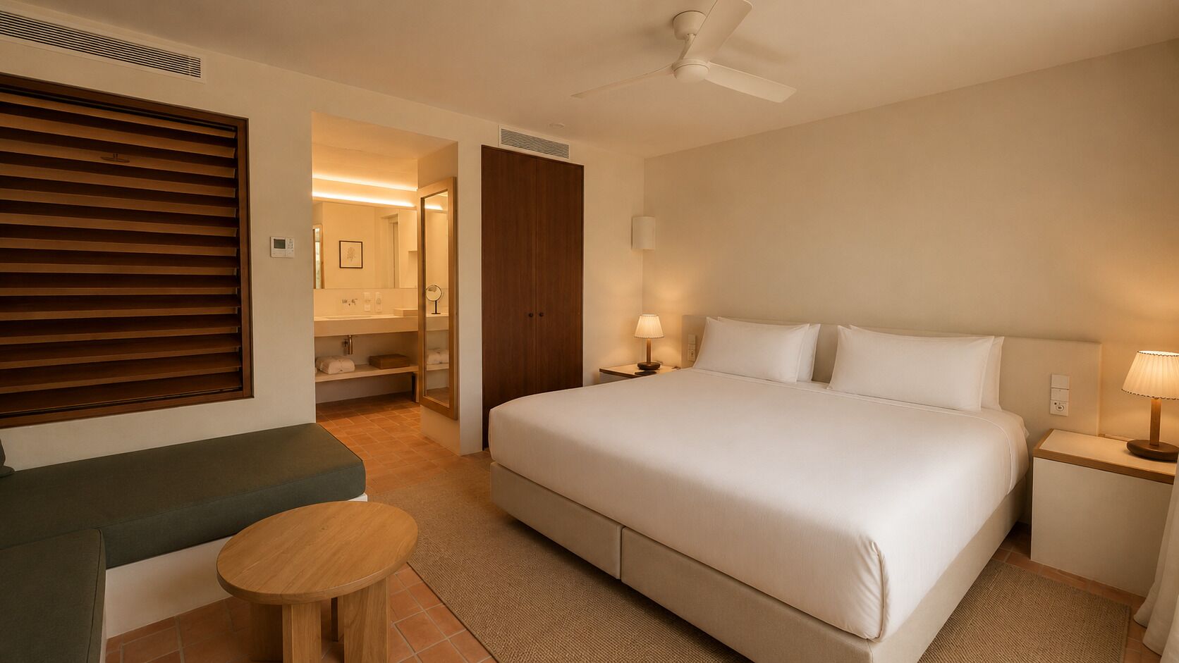 Una habitación de hotel con cama, mesitas de noche, zona de estar y baño visible a través de una puerta abierta.