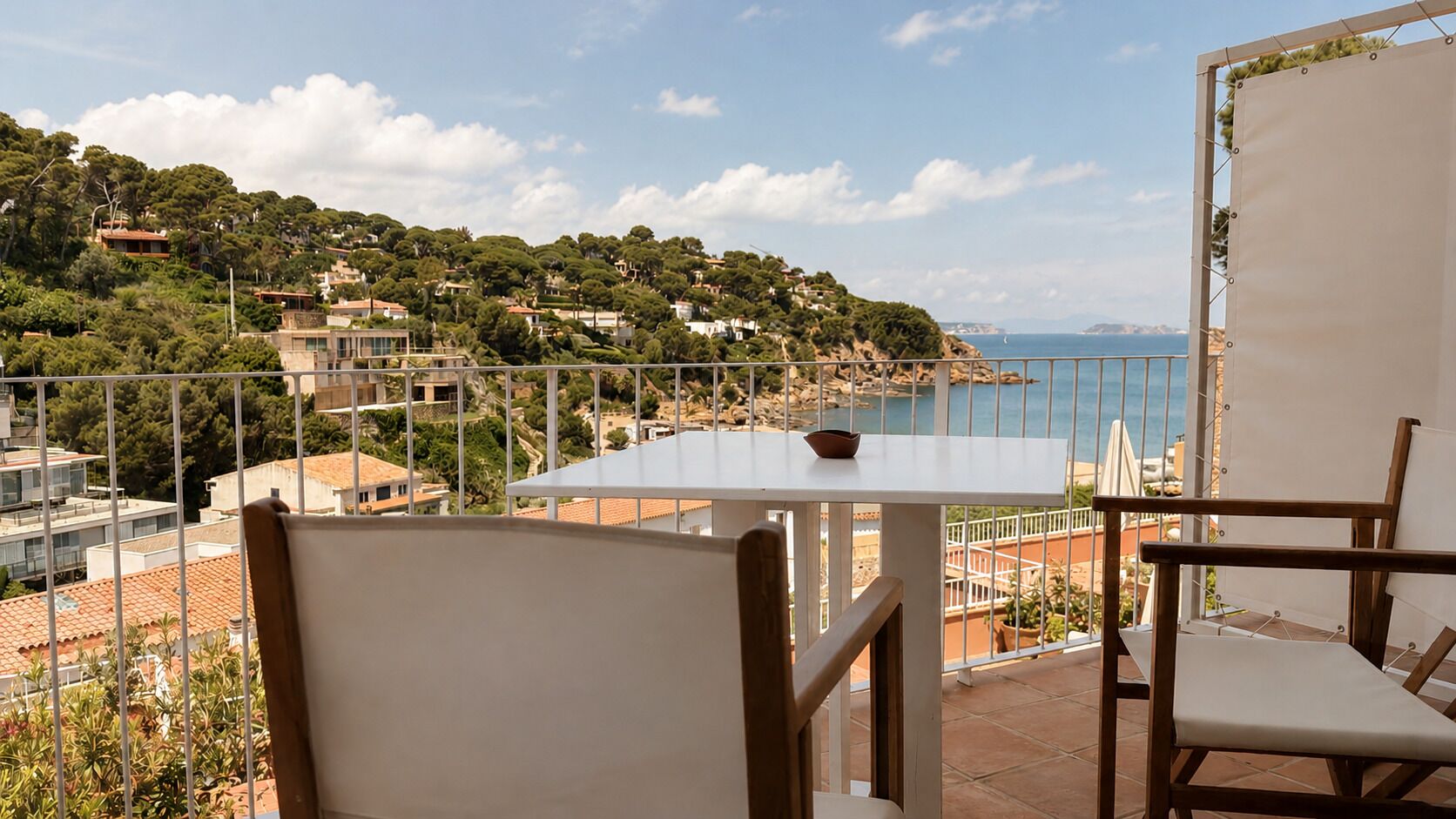 Balcón con mesa y sillas con vista al mar, casas y árboles.