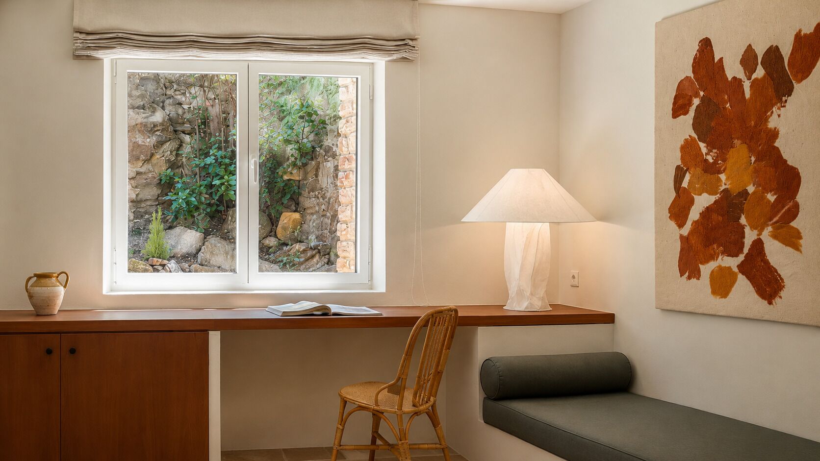 Une pièce comprenant un bureau, une chaise et un banc, une fenêtre donnant sur un espace verdoyant et une lampe fixée au mur.