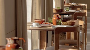 A dining area with wooden tables and chairs, a window with curtains, and various dishes and utensils on the tables. - Finca Victoria Hotel & Spa (Begur)