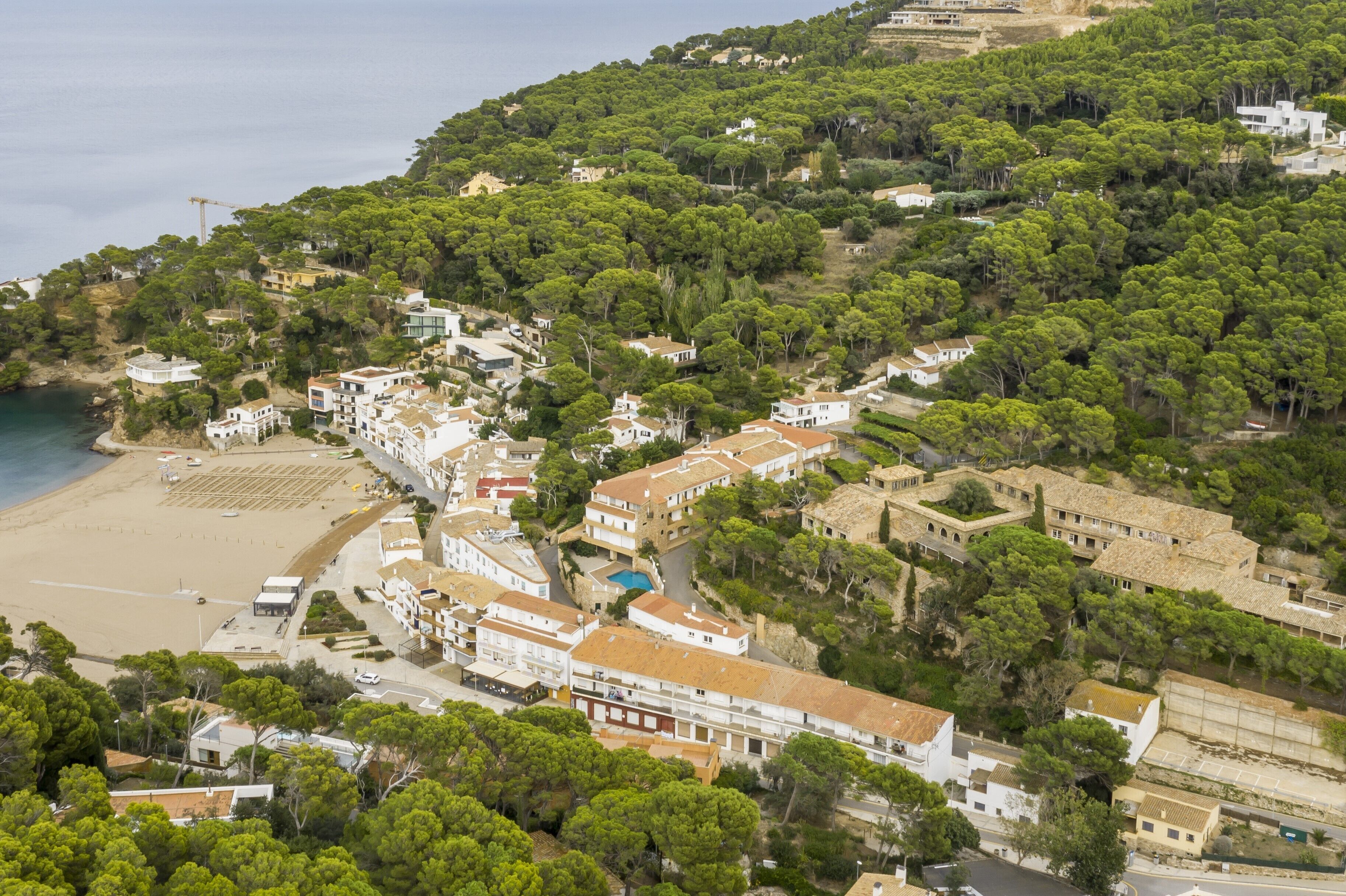 Vista aérea de un pueblo costero con edificios, una playa y abundante vegetación.