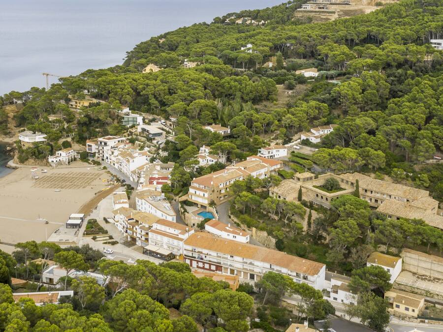 Vista aérea de un pueblo costero con edificios, una playa y abundante vegetación.