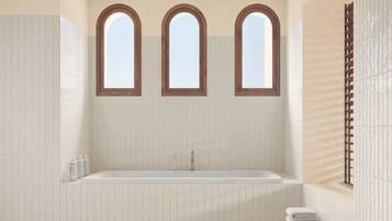 Un baño moderno con una bañera independiente, tres ventanas arqueadas y un perchero para toallas.