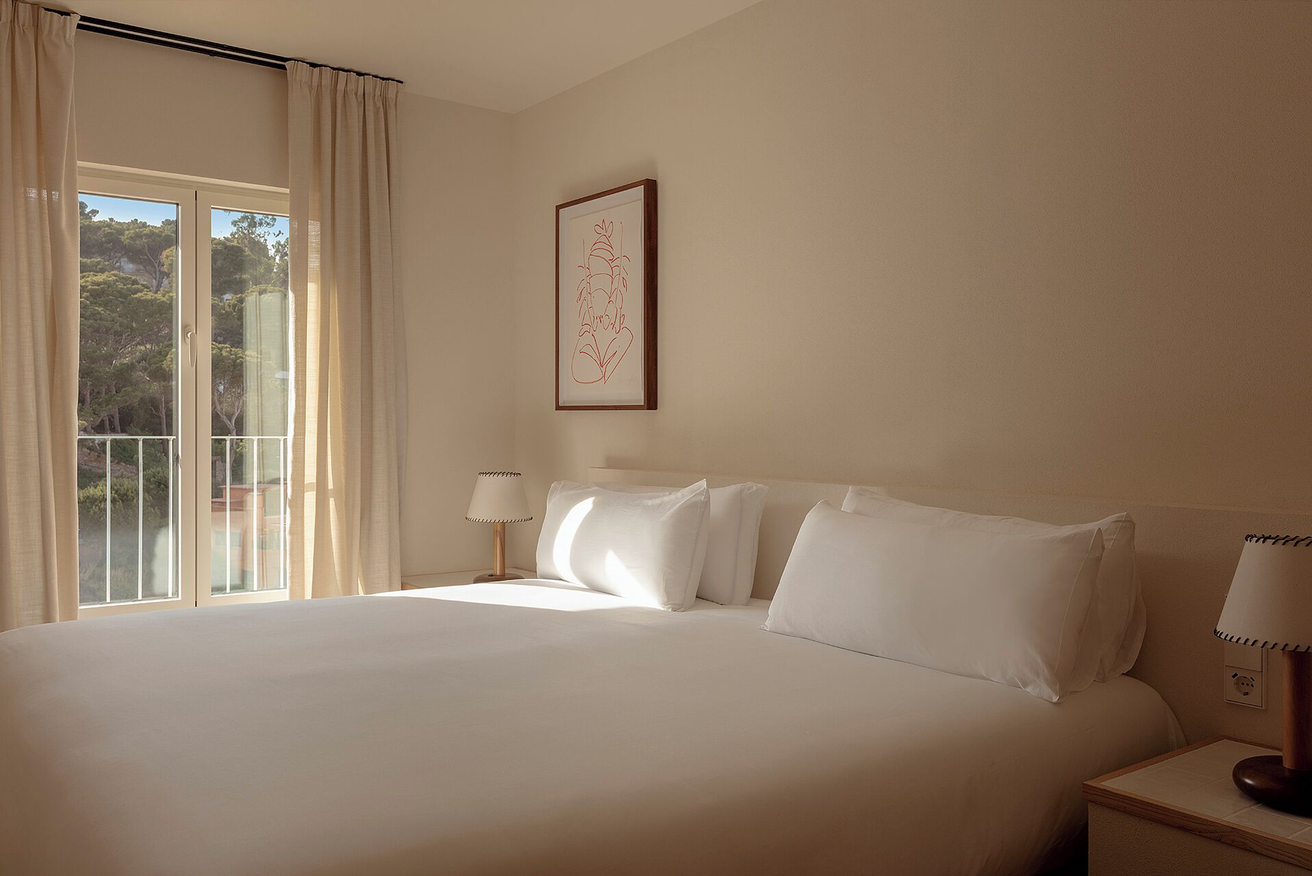 Ein Hotelzimmer mit einem großen Bett, einem Fenster mit Vorhängen, einem Nachttisch mit Lampe und einem gerahmten Bild an der Wand.