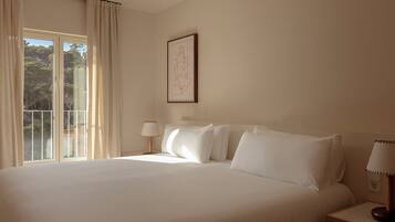 Camera d'albergo con un letto grande, una finestra con tende, un comodino con una lampada e un quadro incorniciato appeso al muro.