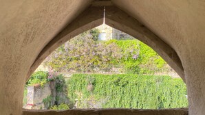 An arched window with a view of a garden and a stone building.
